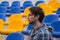 Attractive sporty young man model in blue shirt sitting on blue stadium seats after training staring at field