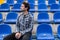 Attractive sporty young man model in blue shirt sitting on blue stadium seats after training staring at field