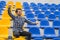 Attractive sporty young man model in blue shirt sitting on blue stadium seats after training staring at field