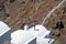 Attractive tall woman battles the wind standing on top of curved roof of white typically Greek Island building against harsh