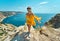 Attractive tanned smiling woman making step on cliff edge against beautiful sea view. Carefree female in bright yellow