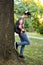 Attractive teenage boy in checkered shirt, blue jeans, sunglasses and baseball cap lean on a tree waiting for someone or