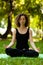 Attractive and tranquil woman sits in lotus position under tree. Yoga and meditation, concentration and relaxation, unity with