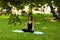 Attractive and tranquil woman sits in lotus position under tree. Yoga and meditation, concentration and relaxation, unity with