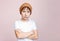 Attractive tween unhappy boy with dark hair in hat looks at camera isolated on light pink background
