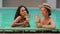 Attractive two female friend caucasian and arabian women people model drink tropical alcohol cocktails in bar on water