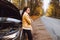 Attractive upset afro haired brunette beside of her broken car in the forest on empty road