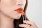 Attractive woman applying orange lipstick