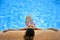 Attractive woman in bikini and sunglasses sunbathing leaning on edge of holidays resort swimming pool