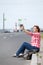 Attractive woman blogging with smartphone while sitting road border in city, an empty highway