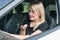 Attractive woman with blond hair sits behind the wheel of a car and speaks indignantly on the phone