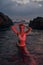 Attractive woman enjoys nocturnal swim in sea illuminated by crimson light. Nighttime ocean dip by stylish female