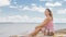 Attractive woman in a hat sits on the beach against the blue sea.