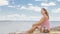 Attractive woman in a hat sits on the beach against the blue sea.