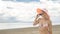 Attractive woman in a hat stands on the beach against the blue sea.