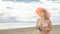 Attractive woman in a hat stands on the beach against the blue sea.