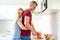 attractive woman hugs her husband while he cuts red watermelon in their large contemporary white kitchen