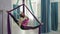 Attractive woman practices antigravity yoga in hammock in studio.