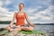 Attractive woman is practicing yoga on the stone near beautiful river.