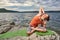 Attractive woman is practicing yoga on the stone near beautiful river.