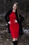 Attractive woman in red dress and black coat standing in winter park