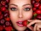 Attractive woman tasting cherry and strawberry. Beautiful woman with fashion makeup and a vivid background