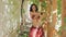 Attractive woman with tattoos dancing belly dance in gazebo overgrown with vines