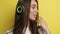 Attractive woman on a yellow background in stylish green headphones listens to music and smiles at the camera. Active