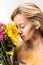 attractive woman with yellow paint on body sniffing bouquet of flowers