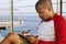 Attractive young African-American hipster man relaxing on the beach and making travel notes in paper notebook.