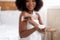 Attractive young Afro woman applying cream on body, pampering herself after bath or shower at home
