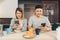 Attractive young Asian couple distracted at table with newspaper and cell phone while eating breakfast.
