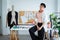 Attractive young Asian LGBTQ gay dressmaker sitting pose on working desk, confident looking at camera, sketch of fashion dress