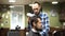 Attractive young barber is cutting human hair with the scissors. He is looking at hair with concentration. The bearded