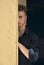 Attractive young blond man hiding half face behind wall