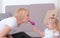 Attractive young blond mom inflate a balloon for her charming daughter sitting near the sofa. Family pastime.