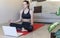 Attractive young brunette doing exercise at home watching videos in the laptop while standing on a gym mat. Doing yoga meditation