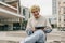 Attractive young caucasian man smiling in camera, using tablet sitting in yard of univercity.