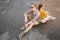 An attractive young couple in sunglasses sit back to back on their longboard in a suburban parking lot against a gray