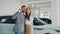 Attractive young couple is taking selfie with car keys in modern motor showroom after buying new automobile. They are