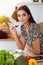 An attractive young dark-haired woman tastes a new recipe for a delicious salad mix while sitting at the table in sunny