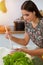 An attractive young dark-haired woman tastes a new recipe for a delicious salad mix while sitting at the table in sunny