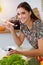 An attractive young dark-haired woman tastes a new recipe for a delicious salad mix while sitting at the table in sunny