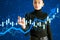 Attractive young european woman using creative blue candlestick forex chart and growing arrow on blue background. Trade, finance