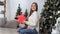 Attractive young female smiling holding red gift box near christmas tree. Wide shot on RED camera