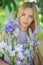 Attractive young girl with blonde dren hair and natural make-up smelling blue purple iris flowers on a background outdoors, tender