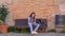 Attractive young girl sitting alone on the banch with mobile phone and backpack. Bored teen scrolling, sending message