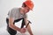 Attractive young guy. Man in casual clothes and orange colored hard hat have some work using hammer. White background