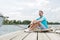 Attractive young guy sits in blue polo on pier near the yacht. smiled tourist handsome man relaxing and enjoying the view on pier