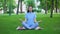 Attractive young lady meditating in park sitting lotus pose, relaxing outdoors